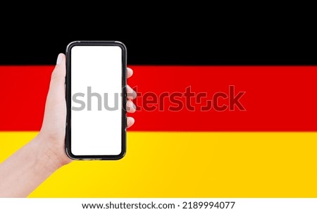 Close-up of male hand holding smartphone with blank on screen, on background of blurred flag of Germany.