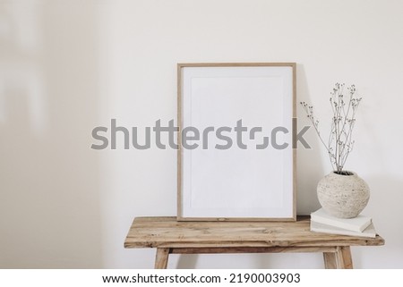 Winter, fall still life. Dry grass, plant bouquet in rustic ceramic vase. Old books on wooden bench. Blank vertical picture frame mockup. White wall background. Empty copy space. Scandinavian nterior