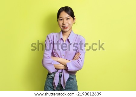 Cheerful Asian Millennial Lady Crossing Hands Posing Smiling Looking At Camera Standing Over Yellow Background In Studio. Female Beauty, Fashion And Self Confidence Concept