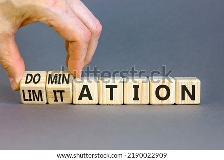 Domination or limitation symbol. Businessman turns cubes, changes the word domination to limitation. Beautiful grey table, grey background, copy space. Business, domination or limitation concept. Royalty-Free Stock Photo #2190022909
