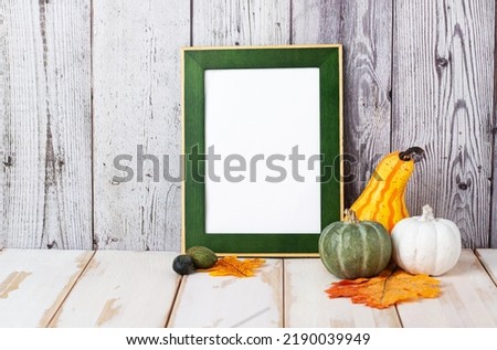 Autumn and Halloween concept. Portrait frame against a light wall with fallen leaves. Frame with pumpkins and space for text.