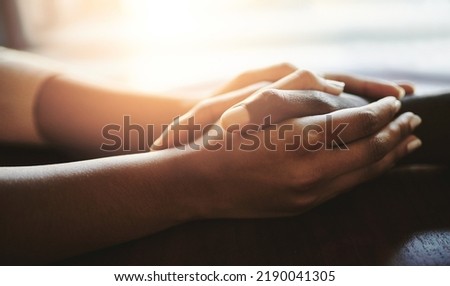 Couple comforting, supporting and holding hands on a table. An African man and woman showing love, compassion and romance in a gesture of care. Human connection through touch, helps with grief. Royalty-Free Stock Photo #2190041305
