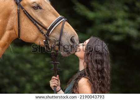A female equestrian cuddles with her bridled kinsky horse. Portrait of a young woman giving a little kiss on her horses nose Royalty-Free Stock Photo #2190043793