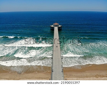 Aerial picture of couple walking on empty pier of Manhattan Beach in California. Drone shot of sandy beach and blue skies. Summer on the American west coast USA. Picturesque post card image of ocean
