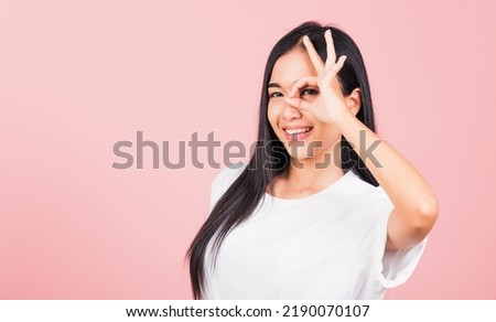Portrait Asian beautiful young woman standing, She made finger OK symbol sign to agree near eyes looking at camera, studio shot isolated on pink background, Thai female agree hand sign copy space