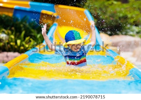 Kids on water slide in aqua park. Children having fun on water slides on family summer vacation in tropical resort. Amusement park with wet playground for young child and baby. Royalty-Free Stock Photo #2190078715
