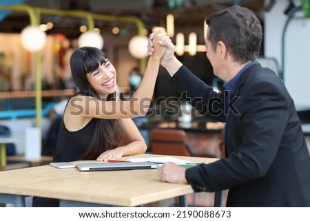 Collaborative process of professional businesspeople shaking hands after new business contract signed, using computer and smart mobile phone with happy face. Coworker and working together concept