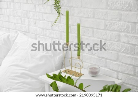 Holder with green candles on table in bedroom
