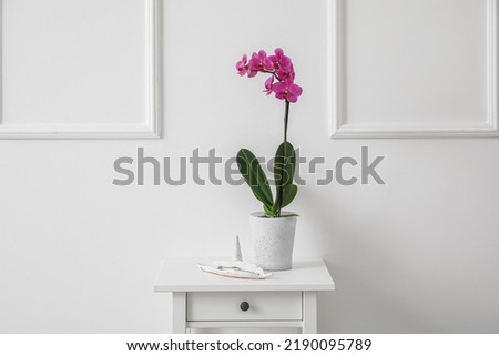 Beautiful orchid flower and tray with jewelry on table near white wall Royalty-Free Stock Photo #2190095789