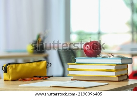 Apple with school books, eyeglasses and pencil case on table in classroom