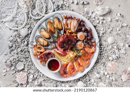 Mussels in shells, squid in a bowl, octopus, shrimps with lemon, thyme and onions in a plate standing on a white wooden table with shells and stones Royalty-Free Stock Photo #2190120867