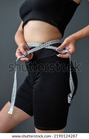 A young smiling woman measures her ideal waist with a tape measure and shows the result of her diet. Weight loss - portrait of a happy fitness girl. isolated body on gray background