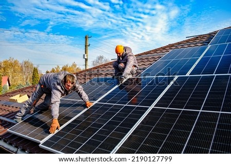 Solar panel technician installing solar panels on roof. technician in blue suit installing photovoltaic blue solar modules. Electrician panel sun sustainable resources Royalty-Free Stock Photo #2190127799