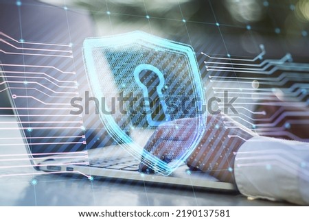 Close up of businessman hands using laptop on desktop with coffee cup and creative glowing shield circuit security hologram on blurry background. Safety and web protection concept. Double exposure