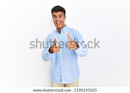 Young hispanic man wearing business shirt standing over isolated background pointing fingers to camera with happy and funny face. good energy and vibes. 
