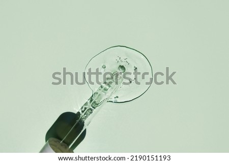 Transparent drop of aloe vera gel and a glass pipette on a green background. Flat lay, space for text.