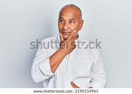 Middle age latin man wearing casual clothes with hand on chin thinking about question, pensive expression. smiling with thoughtful face. doubt concept.  Royalty-Free Stock Photo #2190154965