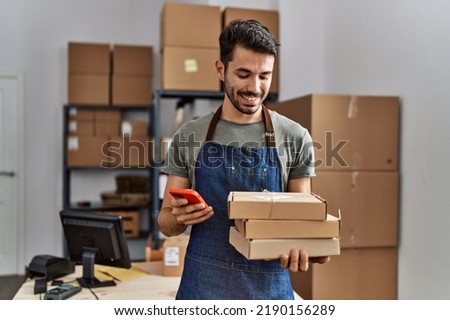 Young hispanic man business worker using smartphone holding packages at storehouse Royalty-Free Stock Photo #2190156289
