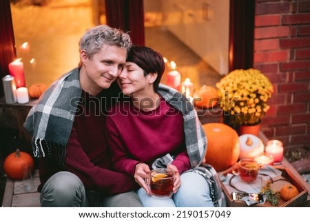 A couple having a romantic date on the porch of their home. Cozy ideas on how to spend time at home. Autumn tea time outdoors on house entrance decorated with pumpkins, flowers and burning candles
