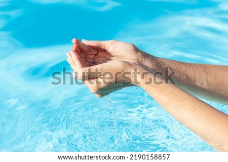 Female hand with vacation blue nail design. Glitter aquamarine nail polish manicure. Female model hand with perfect aquamarine manicure in a light blue pool water.
