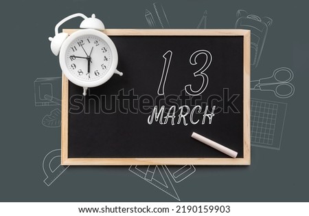 march 13. 13th day of month, calendar date. Blackboard with piece of chalk and white alarm clock on green background. Concept of day of year, time planner, spring month