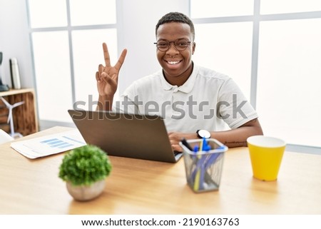 Young african man working at the office using computer laptop showing and pointing up with fingers number two while smiling confident and happy. 