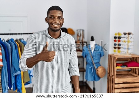 Young african american man working as manager at retail boutique doing happy thumbs up gesture with hand. approving expression looking at the camera showing success. 