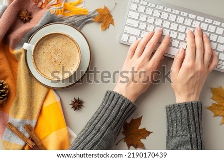 Autumn concept. First person top view photo of female hands in sweater typing on keyboard cup of coffee on saucer plaid yellow maple leaves anise pine cone cinnamon sticks on isolated grey background