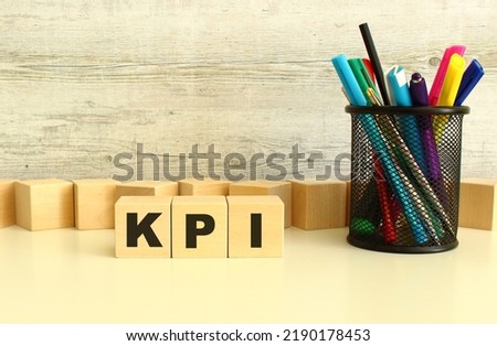 Three stacked wooden cubes with letters KPI on a white desktop on a gray background. Business concept