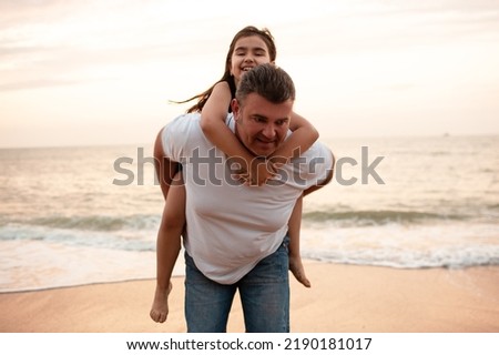 Father and daughter walk on the beach, have fun and hugging on the a sandy beach against the background of the sea or ocean. Man holding a kid in his arms