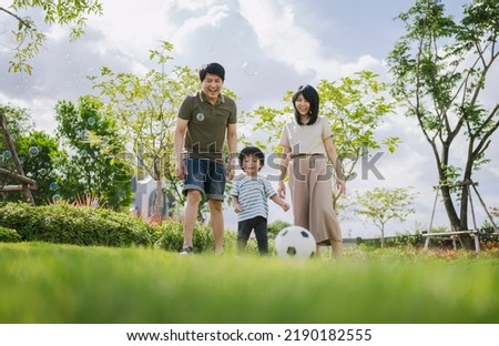 Asian parents and little boy playing soccer in the park together. Happy family life concept. 
