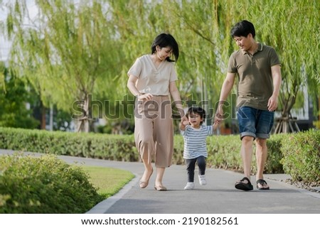 Happy beautiful family of three holding hands while walking in the park. Parents spending time with their children outside. 
