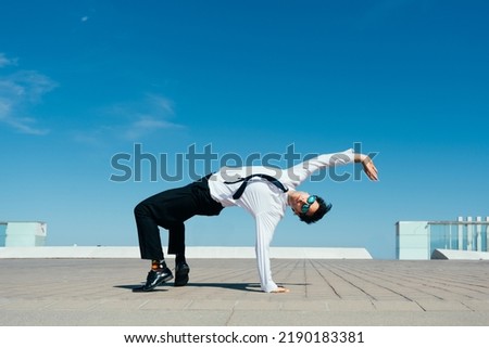 Happy and handsome adult businessman wearing elegant suit doing acrobatic trick moves in the city, alternative concept for business advertisement with energetic and creative people Royalty-Free Stock Photo #2190183381