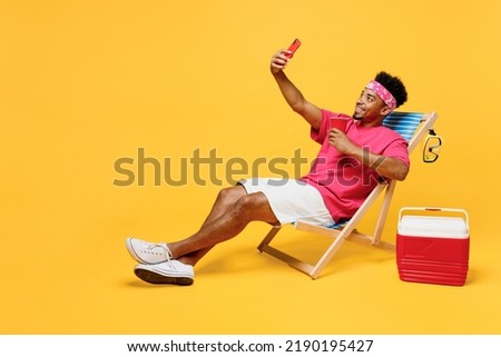 Full body young fun man he wear pink t-shirt bandana near hotel pool doing selfie shot on mobile cell phone drink soda pop water isolated on plain yellow background. Summer vacation sea rest concept