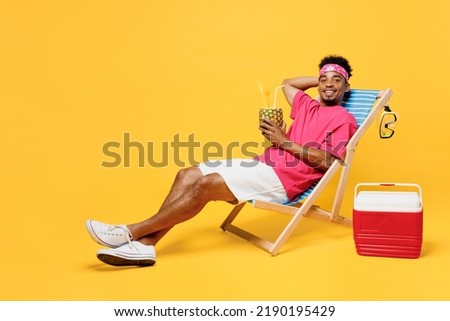 Full size young man he wear pink t-shirt bandana lying on deckchair near hotel pool drink pineapple juice hold hand behind neck isolated on plain yellow background. Summer vacation sea rest concept Royalty-Free Stock Photo #2190195429