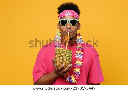 Young fun stylish man 20s he wearing pink t-shirt sunglasses hawaiian lei near hotel pool drink straw pineapple juice look camera isolated on plain yellow background. Summer vacation sea rest concept Royalty-Free Stock Photo #2190195449