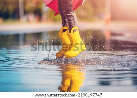 Child jumping in the puddle in yellow rubber boots Royalty-Free Stock Photo #2190197747