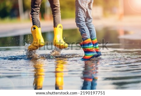 Children jumping in the puddle in rubber boots. Royalty-Free Stock Photo #2190197751
