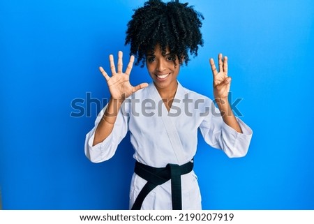 African american woman with afro hair wearing karate kimono and black belt showing and pointing up with fingers number eight while smiling confident and happy. 
