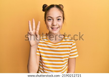 Beautiful brunette little girl wearing casual striped t shirt showing and pointing up with fingers number three while smiling confident and happy.  Royalty-Free Stock Photo #2190212721
