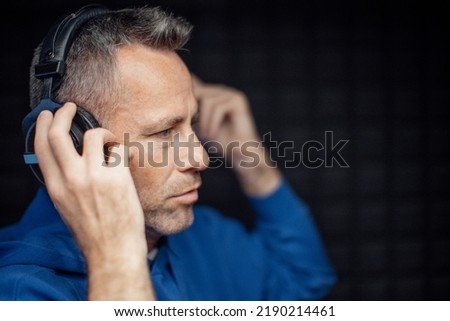 Portrait of mature radio host putting on headphones during making podcast