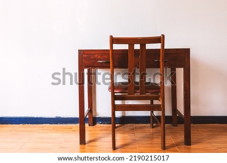 Beautiful vintage wooden table and chair, back side view of the table and chair, table and chair in white room wall and brown floor, no people, natural light with warm tone.