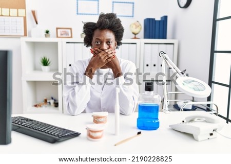 African dentist woman working at medical clinic shocked covering mouth with hands for mistake. secret concept.  Royalty-Free Stock Photo #2190228825