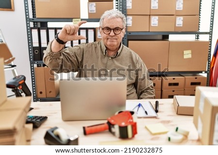 Senior caucasian man working at small business ecommerce with laptop smiling and confident gesturing with hand doing small size sign with fingers looking and the camera. measure concept. 