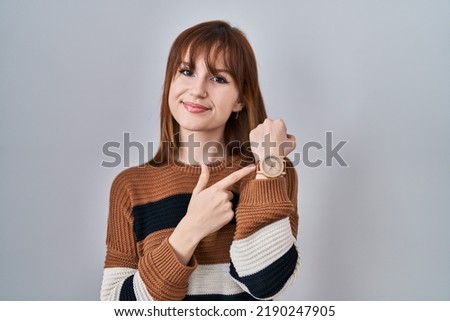 Young beautiful woman wearing striped sweater over isolated background in hurry pointing to watch time, impatience, looking at the camera with relaxed expression 