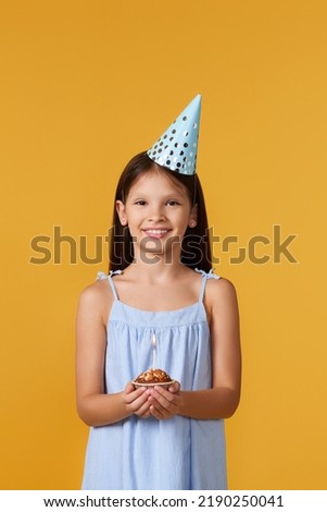 happy little birthday girl with party cone holding cupcake