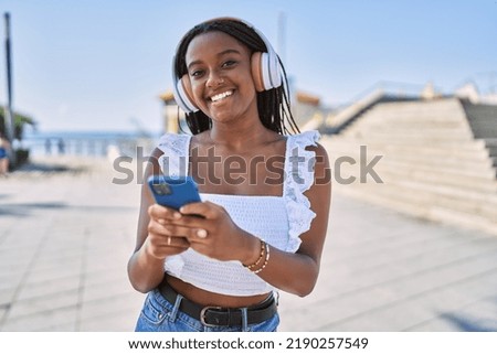 Young african american girl smiling happy using headphones and smaprthone at the city.