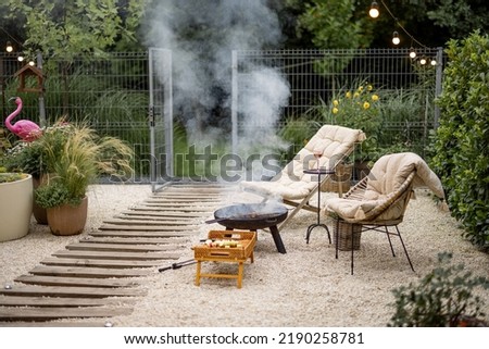 Atmospheric backyard with fire and lounge chairs at dusk on nature. Grilling food on fire bowl