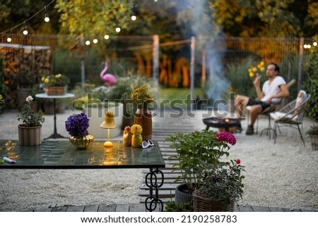 Beautiful and cozy garden with man relaxing sitting by the fireplace on background at dusk