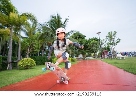 asian child skater or kid girl playing skateboard or surf skate and ollie jumping fun or raise wheel manual in skate park by extreme sports to wear helmet elbow pads wrist knee support for body safety Royalty-Free Stock Photo #2190259113
